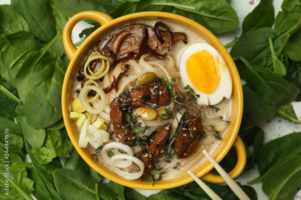 Tasty Chinese soup in pot with herbs on table