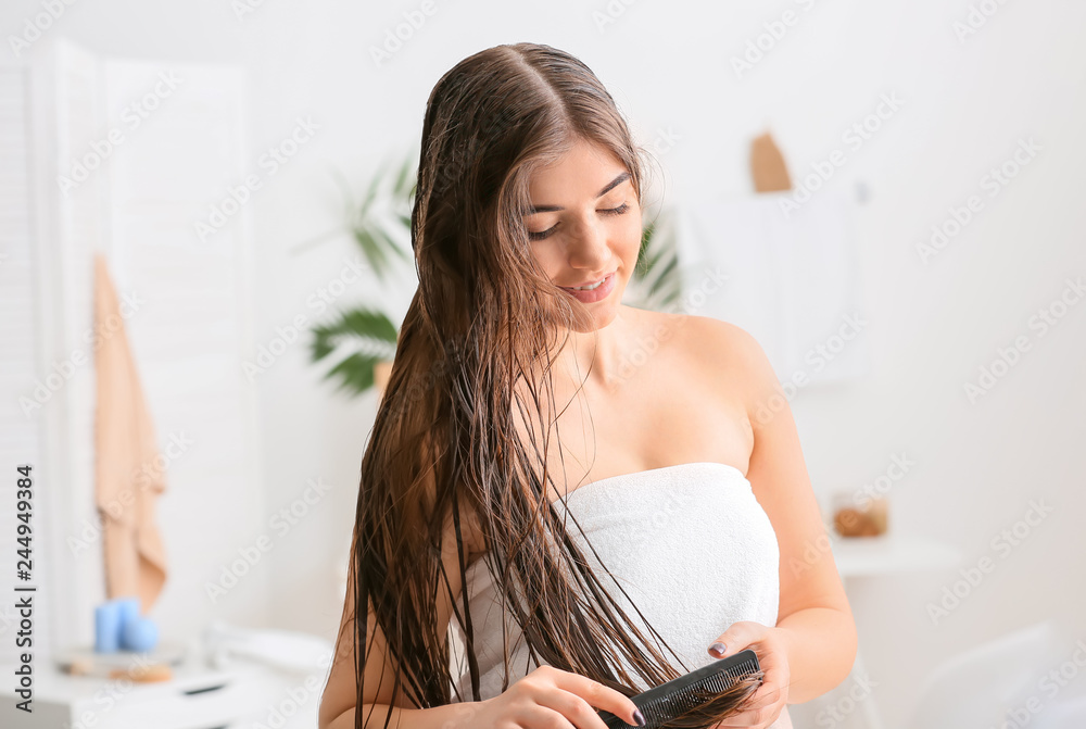 Young woman combing beautiful long hair in bathroom