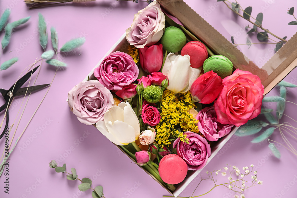 Gift box with beautiful flowers and macarons on color background