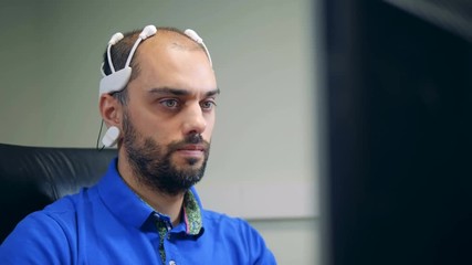 A man in a brainwave scanning headset is operating a computer