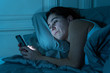 Attractive latin woman addicted to mobile phone and internet late at nigh in bed looking sleepless