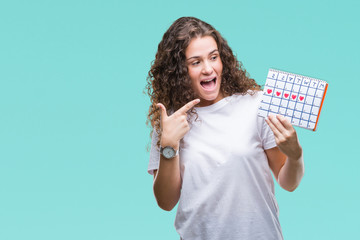 Poster - Young brunette girl holding menstruation calendar over isolated background very happy pointing with hand and finger