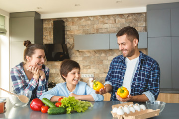 Wall Mural - Family at home standing in kitchen together mother and son smiling cheerful looking at father holding bell peppers playful