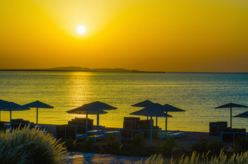 Wall Mural - sunrise, sunset on the beach with umbrellas orange and blue color at dusk.