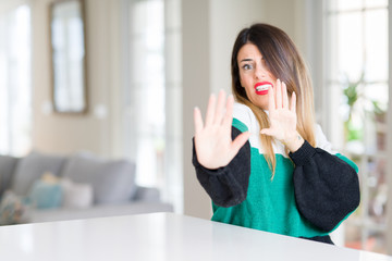 Canvas Print - Young beautiful woman wearing winter sweater at home afraid and terrified with fear expression stop gesture with hands, shouting in shock. Panic concept.