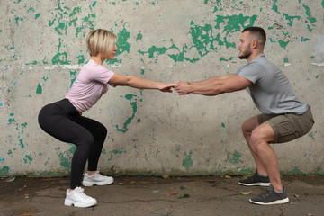 Deep squat. Fitness couple in sportswear doing squat exercises outdoors