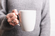 © Olena - Female hand holding white cup in grey sweater background. Copy space