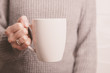 © Olena - Female hand holding white cup in grey sweater background. Copy space