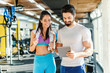 © dusanpetkovic1 - Bearded smiling personal trainer showing woman results of training on tablet. Woman standing next to him and looking at tablet. Gym interior.