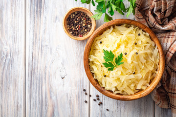 Wall Mural - Homemade sauerkraut with black pepper and parsley in wooden bowl on rustic background. Top view. Copy space.