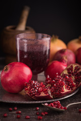 Wall Mural - A glass of pomegranate juice with fresh pomegranate fruits and seeds on rustic background. low key