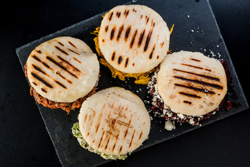 Wall Mural - Venezuelan Latin American food, 4 arepas of different stuffing on a black table. Arepa with mechada meat, queen pepeada, black beans with white cheese and chicken