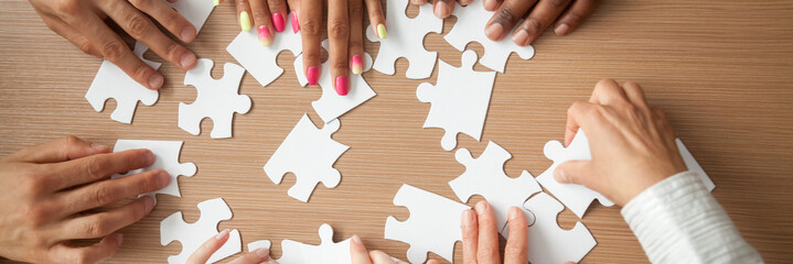 Top above close up hands diverse team assembling jigsaw puzzle joining pieces at desk search right solution, successful teamwork help support concept, horizontal photo banner for website header design