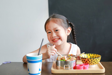 Happy little Asian kid girl eating rice by self in the restaurant.