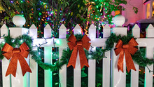 Three Red Christmas Bows And A Green Garland Decorating White Wooden Fence