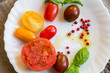 Mixed tomatoes of different colours with herbs and oil on white plate