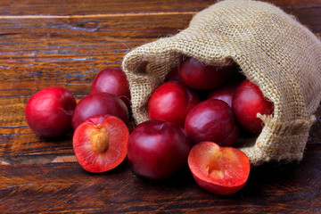 raw and fresh organic plums inside rustic fabric bag on wooden table