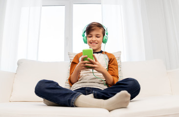 Canvas Print - children, technology and people concept - happy smiling boy with smartphone and headphones listening to music at home