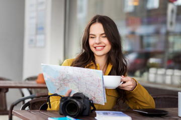 Canvas Print - travel, tourism, leisure and people concept - happy young tourist woman or teenage girl with map and digital camera drinking cocoa at city street cafe terrace