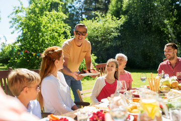 leisure, holidays and people concept - happy family having festive dinner or barbecue party at summer garden