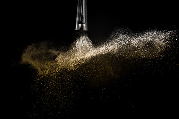 Wall Mural - Cosmetic brush with golden cosmetic powder spreading for makeup artist and graphic design in black background