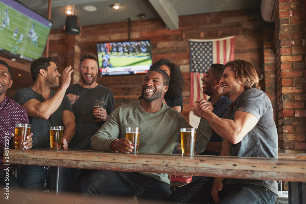 Group Of Friends Watching Game On Screen In Sports Bar - obrazy, fototapety, plakaty 