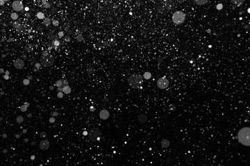 Real snow falling on black background. Falling snow of different shapes and sizes. Blurred snow texture to use as a design element or as an overlay for other photos.