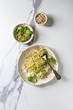 Classic italian spaghetti pasta with pesto sauce, pine nuts, olive oil and fresh basil. Served in ceramic plate with fork and ingredients above over white marble background. Flat lay, space