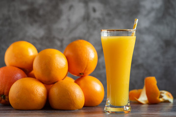 Wall Mural - Glass of freshly squeezed orange juice standing on grey background with a fresh oranges