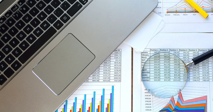 Financial documents - graphics, statistics, drawings, keyboard, laptop, magnifying glass in the office. Business, science, long hours of work.
