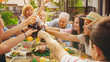 © Gorodenkoff - Family and Friends Gathered Together at the Table Raise Glasses and Bottles To Make a Toast and Clink Glasses. Big Family Garden Party Celebration.