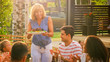 © Gorodenkoff - At the Family Garden Party, Mother Brings Dish with Roasted Bird to the Table. Family and Friends Gathered together at the Big Table. Eating, Drinking and Having Fun.