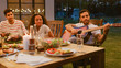 © Gorodenkoff - Sitting at the Dinner Table Handsome Young Man Plays the Guitar For a Friends. Group of Young People Listening to Music at the Summer Evening Garden Party Celebration.