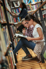 Wall Mural - Two female students read and learns by the book shelf at the library.Reading a book.