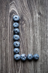 Letter L laid out of blueberry berries on a wooden background