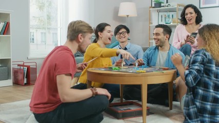 Wall Mural - Diverse Group of Guys and Girls Playing in a Strategic Board Game with Cards and Dice. Reading Cards and Laughing. Friends Having Fun. Cozy Living Room in a Daytime