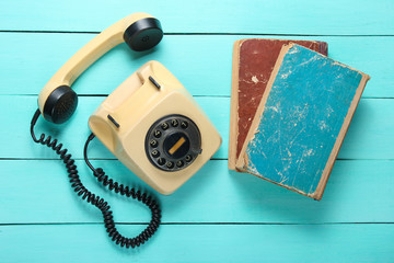 Retro rotary telephone and stack of old phone books on a blue wooden table. Top view