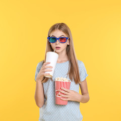 Canvas Print - Emotional teenage girl with 3D glasses, popcorn and beverage during cinema show on color background