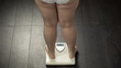 Obese female standing on bathroom scales to check body weight, fat, rear view