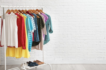 wardrobe rack with stylish clothes and shoes near brick wall indoors. space for text