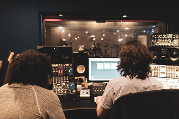 Music Engineer and Artist in Music Recording studio at mixing consol recording hip hop music viewing artists through glass