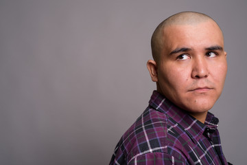 Young bald Asian businessman against gray background