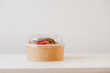 Take away salad in disposable paper bowl on white background. Minimalism food photography concept. Copyspace