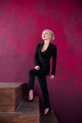 High fashion shot of sexy blond woman in black suit on red background, Portrait of elegantly dressed gorgeous business woman with red lips