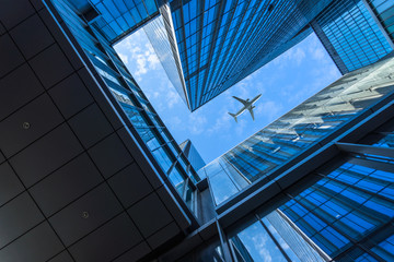 Tall city buildings and a plane flying overhead.