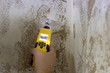 Mit einem Feuchtigkeitsmessgerät wird eine Kellerwand gemessen. Das Messgerät zeigt an, dass die Wand feucht ist.