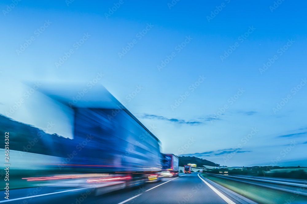 Background photograph of a highway. Truck on a motorway, motion blur, light trails. Evening or night shot of trucks doing logistics and transportation on a highway. - obrazy, fototapety, plakaty 