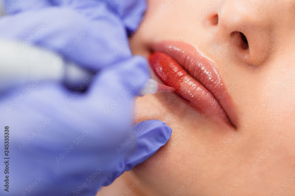 Young woman having permanent makeup on lips in beautician salon. Close up - obrazy, fototapety, plakaty 