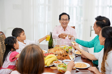 Wall Mural - Adult Asian people with children gathering at table at home while toasting with glasses and having celebration