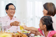 © DragonImages - Adult Asian man and woman with girl at table on family dinner clinking with glasses spending time together